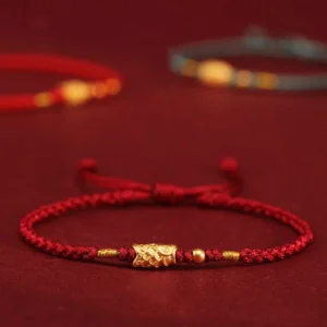 Close-up of 999 gold koi fish charm on red braided string bracelet