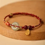 Hetian jade peace buckle koi fish red string bracelet with sterling silver charm on wooden display