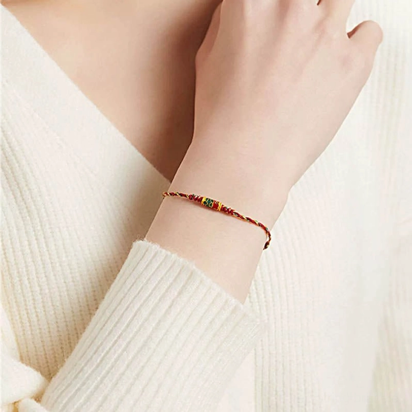 Koi fish red string bracelet worn on wrist with off-white knit sweater close-up view