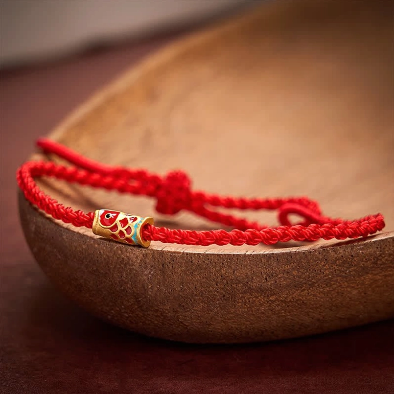 Koi fish charm bracelet close-up on wooden surface showing gold-toned bead and braided red cord