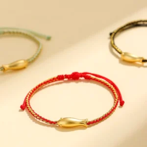 Koi fish red string protection bracelet with gold charm on yellow background flat lay
