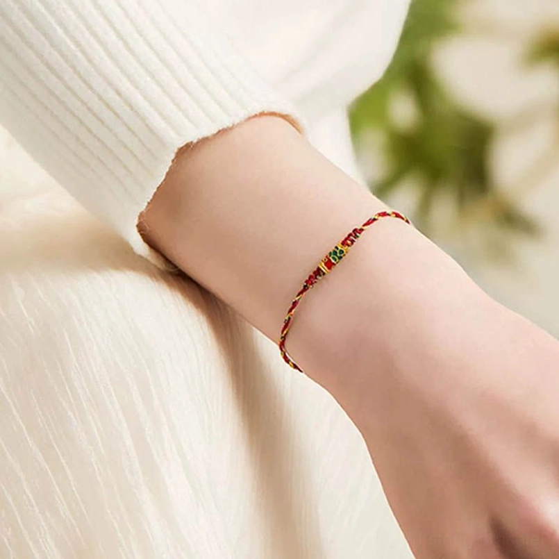 Red braided koi fish prosperity bracelet worn on wrist with green foliage background