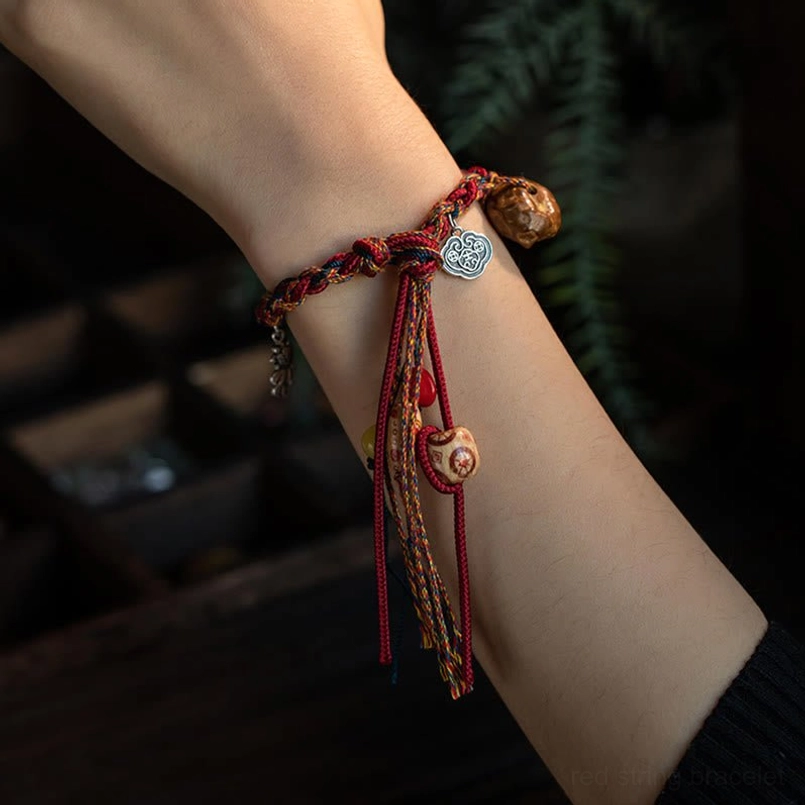 Close-up of handmade red string bracelet worn on wrist with silver cloud charm and natural wood beads