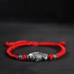 Red woven koi fish sterling silver bracelet with vintage silver charm and decorative beads on dark background
