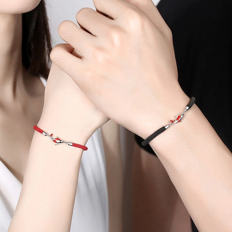 Couple wearing koi fish red and black string bracelets on wrists with minimalist backdrop
