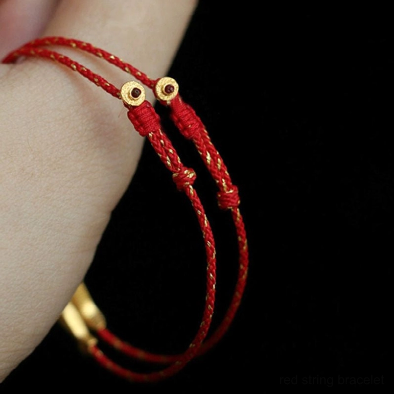 Koi fish red string bracelet worn on wrist with decorative gold round fastener