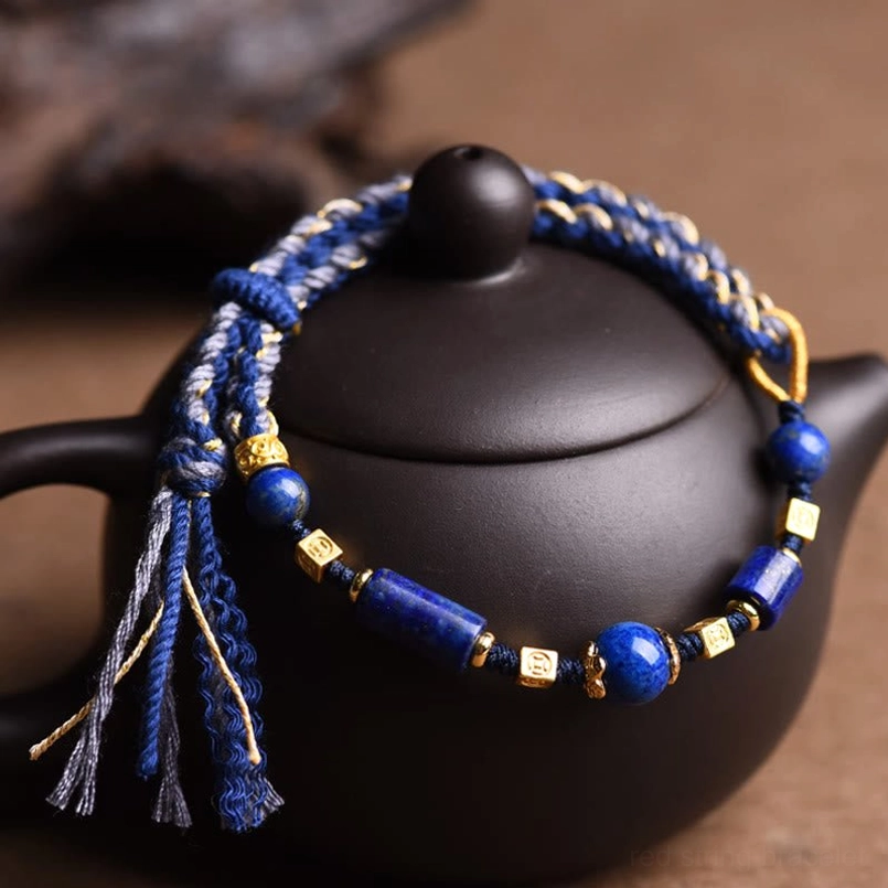 Natural lazurite bead bracelet with hanging tassels displayed on black ceramic