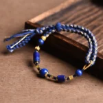 Handmade lapis lazuli red string bracelet with natural lazurite beads and tassel details on wooden tray