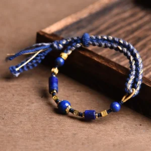 Handmade lapis lazuli red string bracelet with natural lazurite beads and tassel details on wooden tray