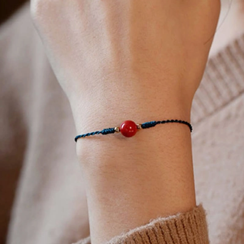 Front close up of cinnabar red string bracelet worn on wrist with large red cinnabar bead