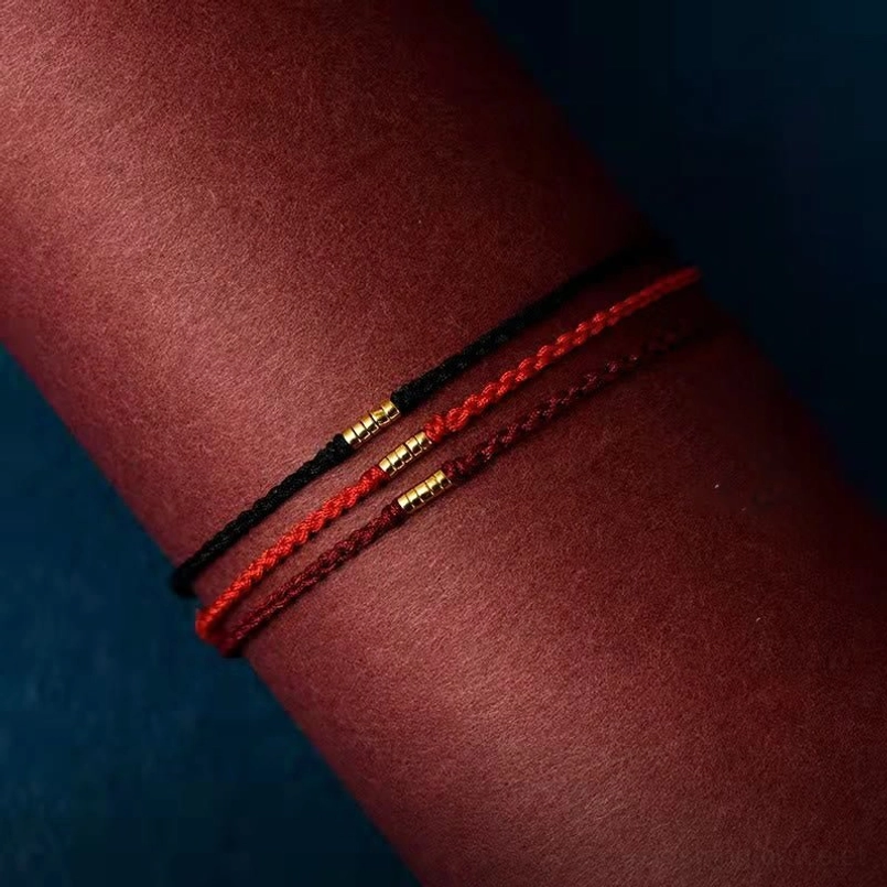 Dual layer red and black braided bracelets with golden beads on dark fabric