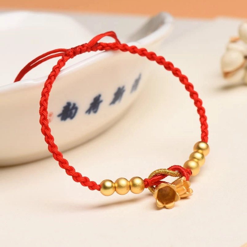 Close-up of red string bracelet with lily pendant and smooth gold beads detail