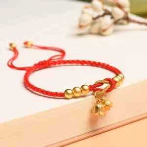Red handcrafted lily of the valley bracelet with gold charm on wooden surface