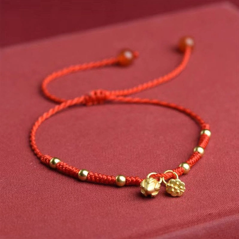 Flat lay of adjustable lotus anklet with dual gold lotus charms and sliding knot on red fabric