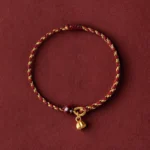 Handcrafted golden lotus pod charm red string bracelet with dark bead accent on dark red backdrop