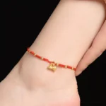 Red lotus pod charm anklet worn on ankle with gold beads on woven string