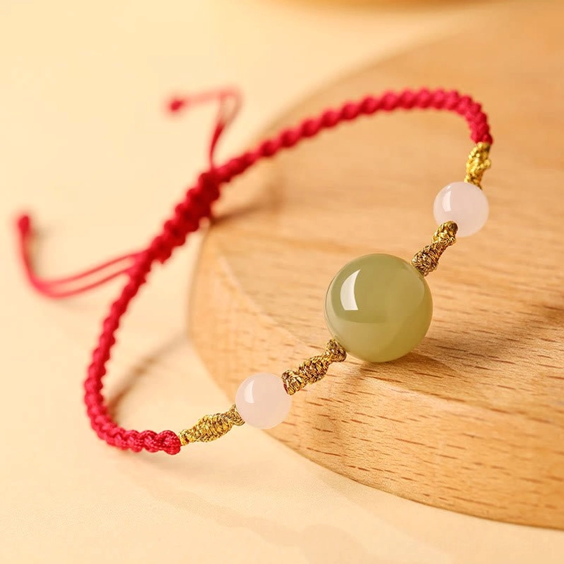 Braided red string lucky bracelet displayed on wooden coaster, oblique angle view