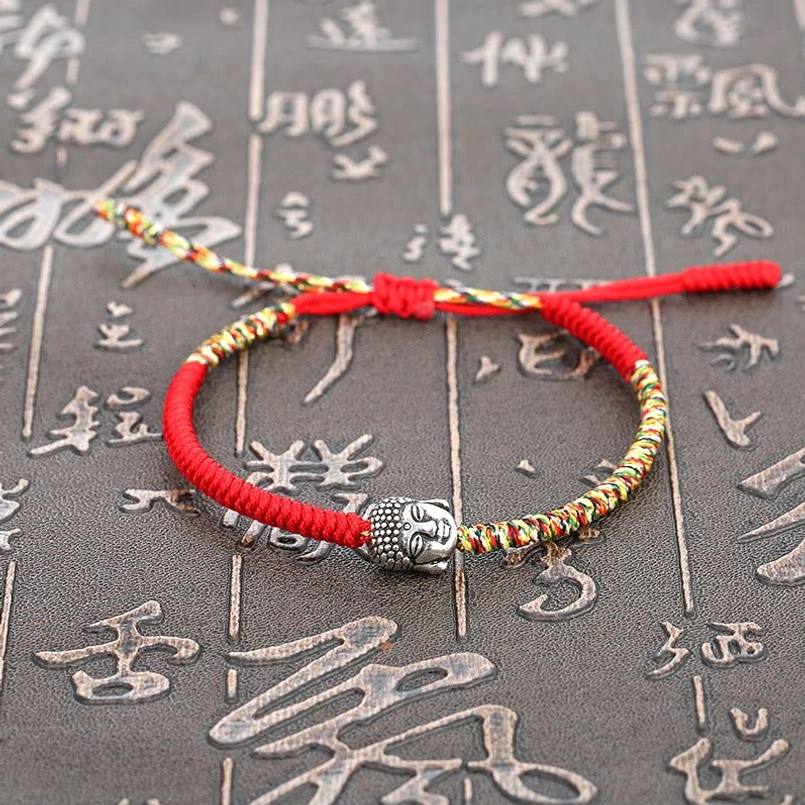 Lucky Buddha charm red string bracelet flat lay on Chinese calligraphy background