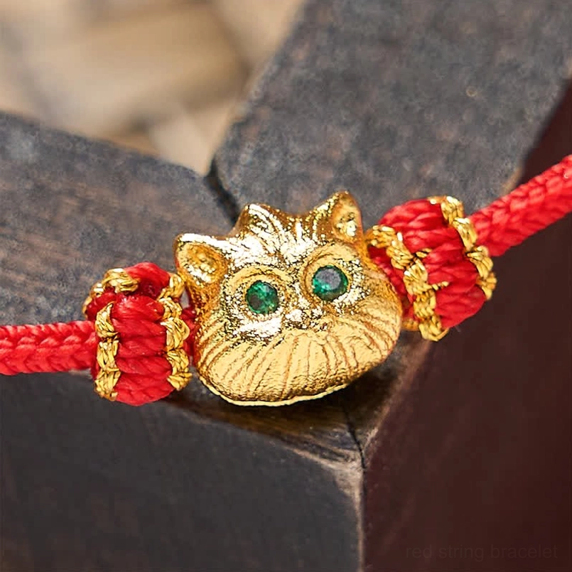 Macro close-up of gold lucky cat charm face with emerald green eyes