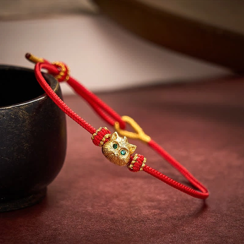 Lucky cat charm pendant with decorative red and gold weave on dark background