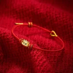 Lucky cat red string bracelet with gold charm and green gem eyes on red fabric