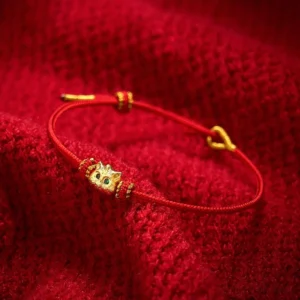 Lucky cat red string bracelet with gold charm and green gem eyes on red fabric