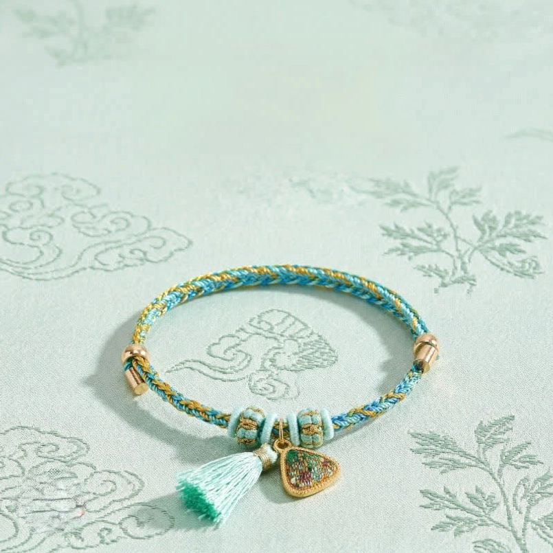 Chinese protection bracelet with braided cord and matching tassel pendant displayed on green background with traditional floral patterns