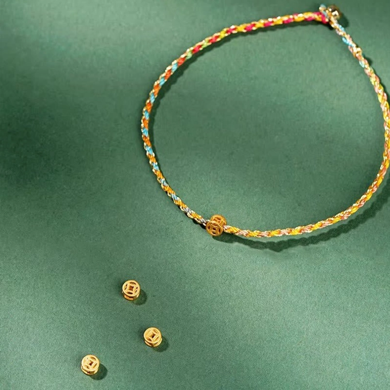 Colorful braided lucky coin bracelet with extra gold coin beads and spare charms in angled view