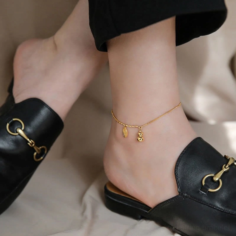 Side view of slim gold lucky gourd anklet with small dangle prosperity pendants