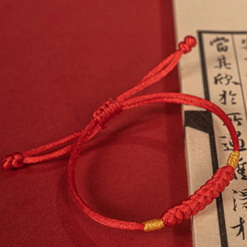 Red string bracelet with gold thread details next to vintage Chinese calligraphy paper