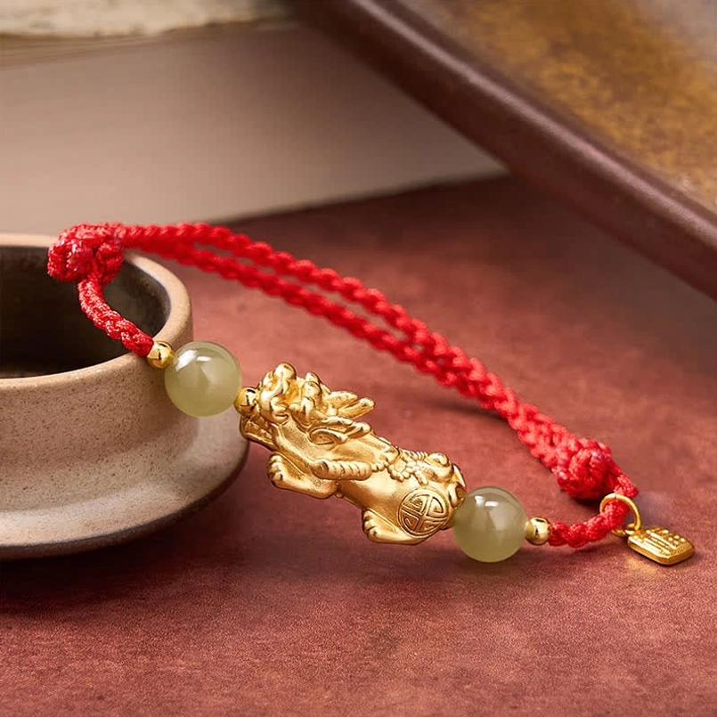 Side flat lay of Pi Xiu Fu Hetian Jade red string bracelet on light red table with ceramic cup