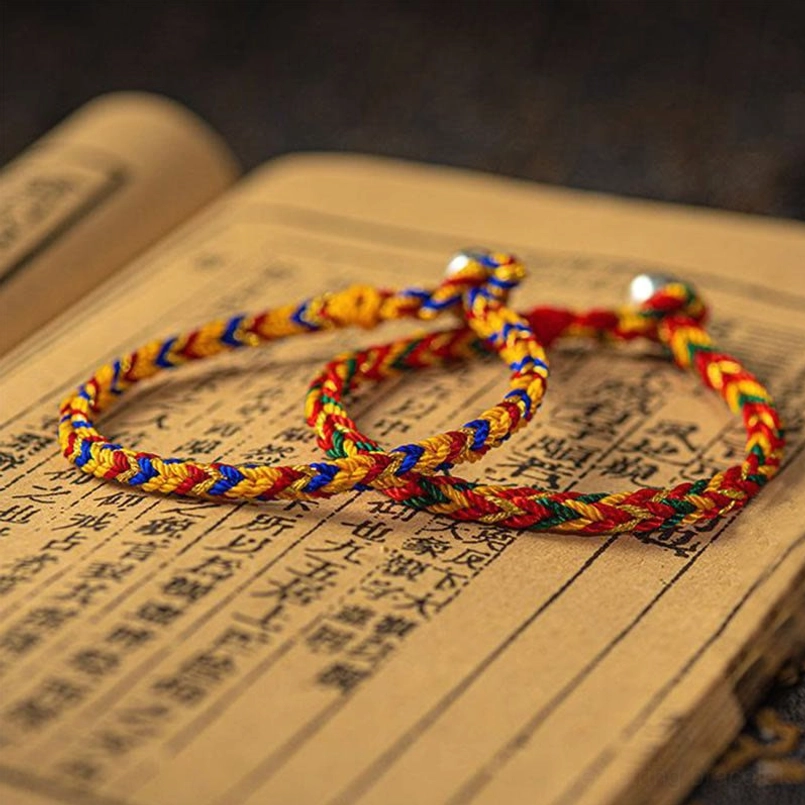 Two handmade woven multicolored bracelets with silver clasp displayed on vintage Chinese book