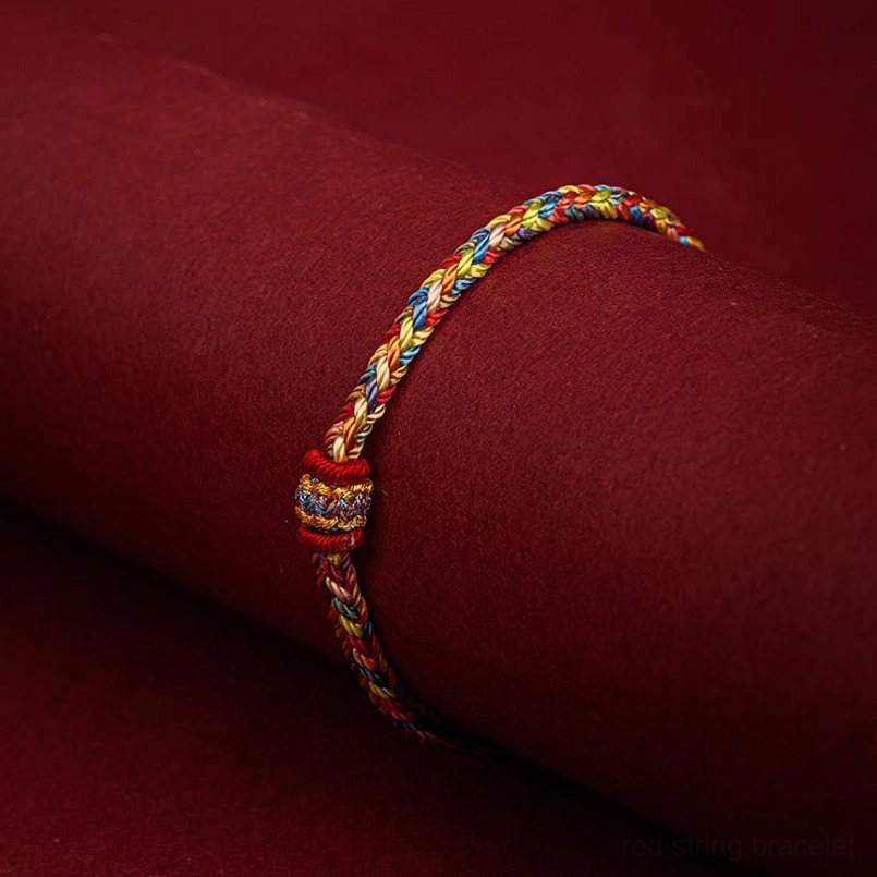 Slim braided handmade lucky bracelet with decorative woven knot displayed on wine red cylinder stand