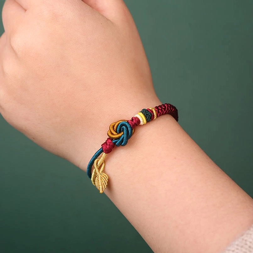 Handmade luck bracelet worn on wrist showing multi-color braided knot and golden leaf pendant