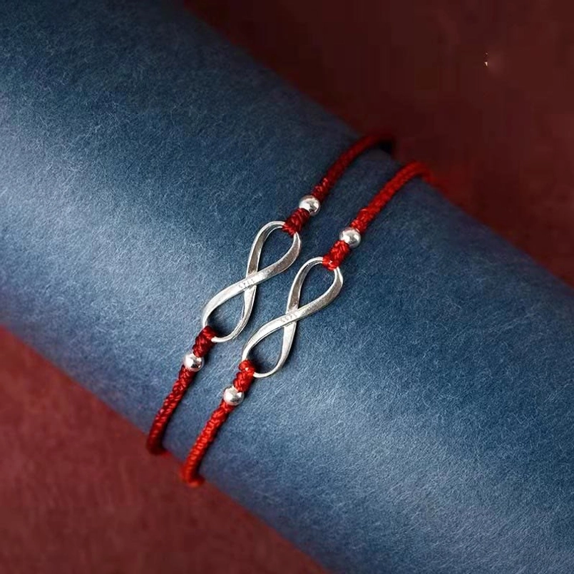 Paired red string bracelets with double infinity knot charms on velvet background