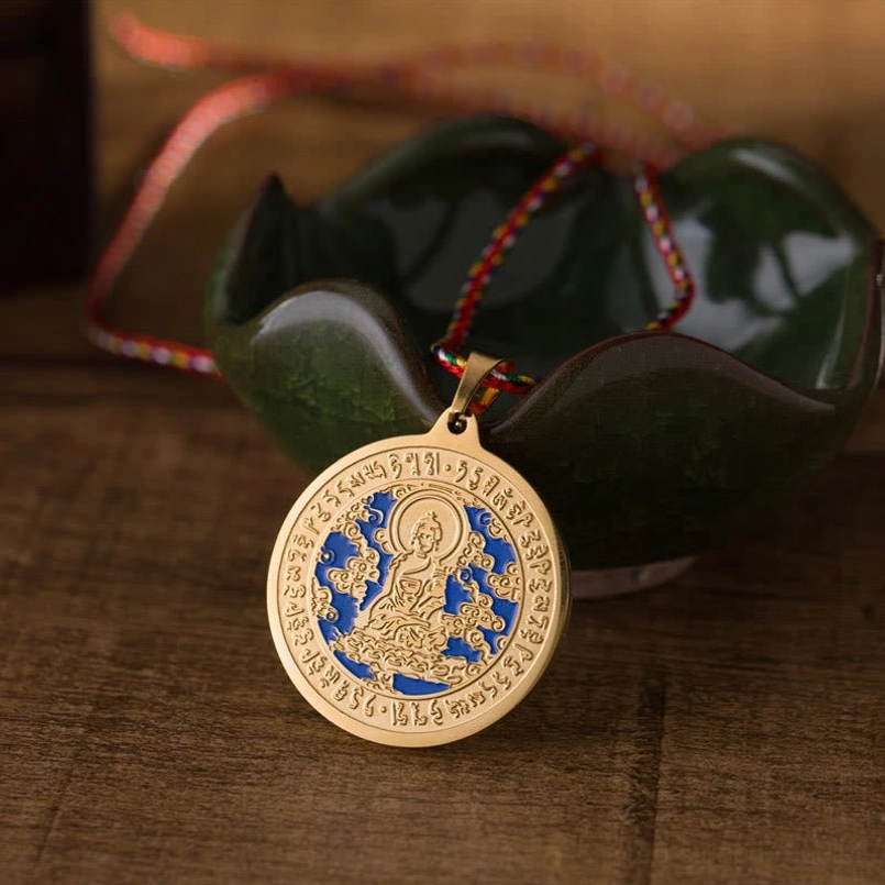 Medicine Buddha blue mantra pendant necklace with gold finish and multicolored braided rope, overhead view on wooden desktop