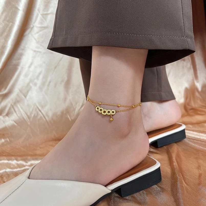 Minimal gold fine chain anklet with tiny copper coin charms and hanging bead detail in lifestyle setting