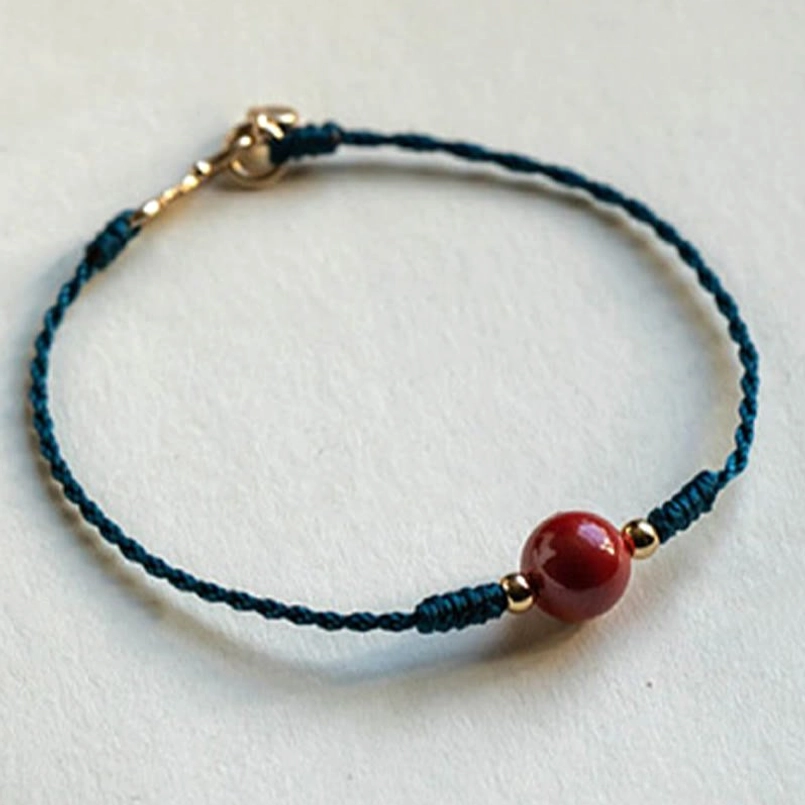 Minimalist slim cinnabar bracelet flat lay on plain off-white fabric background