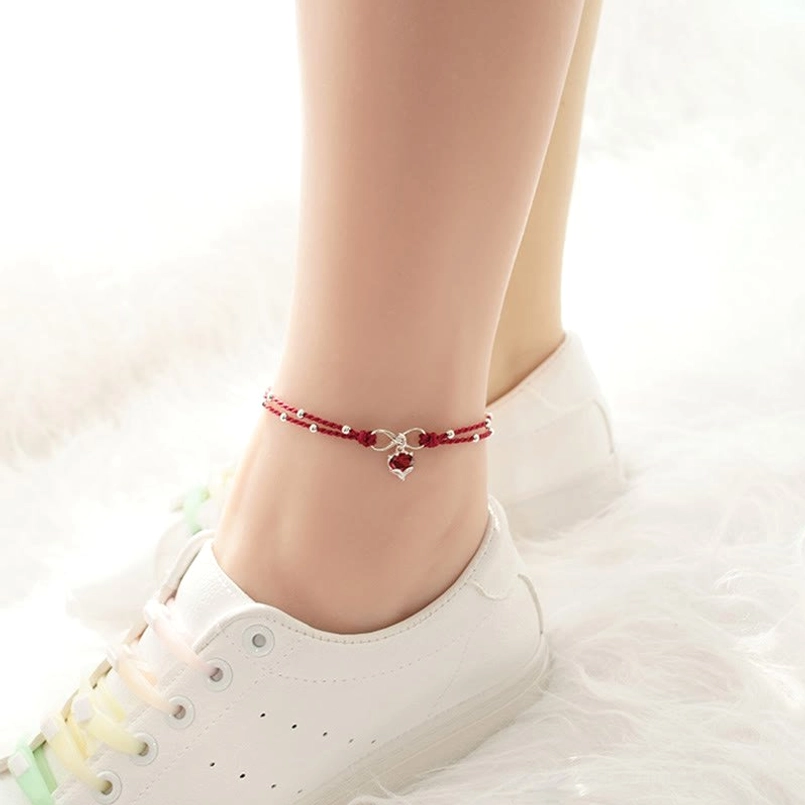 Minimalist red string ankle bracelet with tiny heart charm worn on ankle with white sneaker, casual style