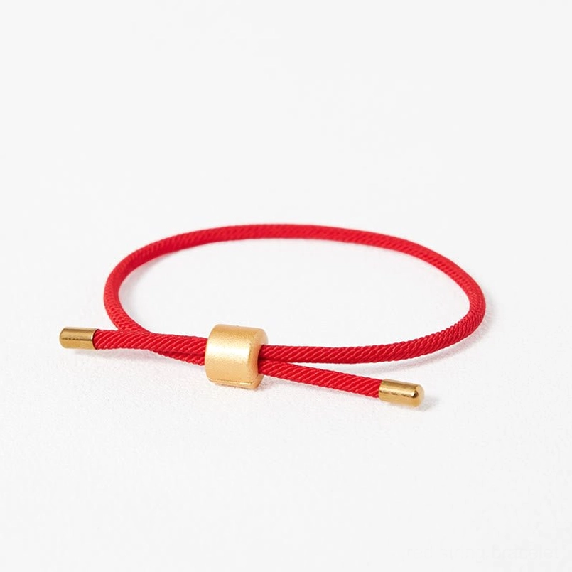 Minimalist red string bracelet top down view with gold clasp white background