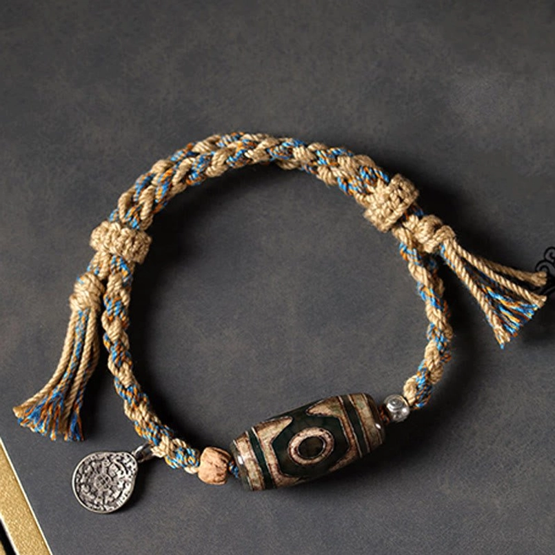 Circular view of blue brown woven Dzi Bead red string bracelet with tassels on dark background