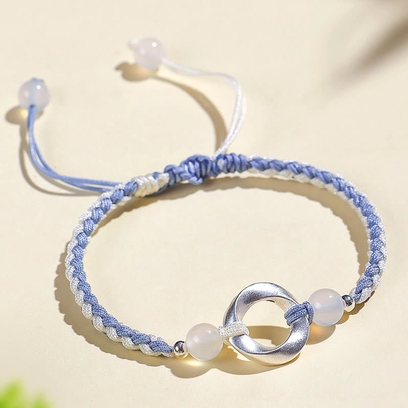 Adjustable red string bracelet with white agate and sterling silver Möbius charm, overhead flat lay photography