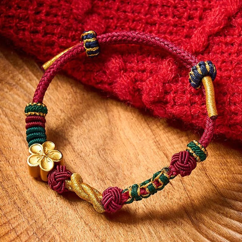 Multicolor Chinese knot couple bracelet with gold four-leaf charm on wooden table