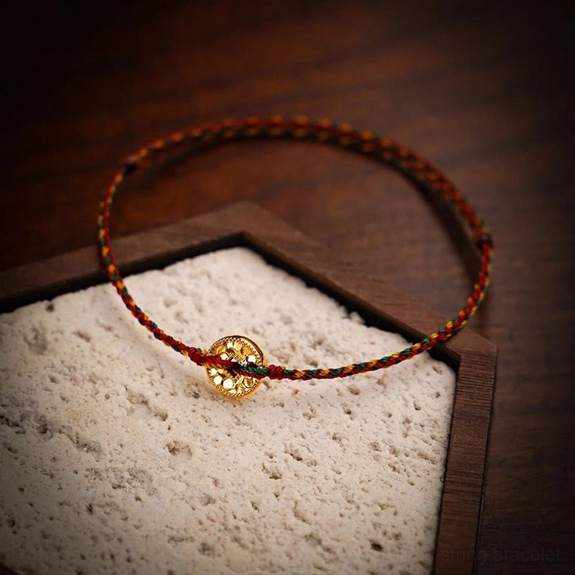 Multicolored braided red string copper coin bracelet on wooden tray with adjustable knot design
