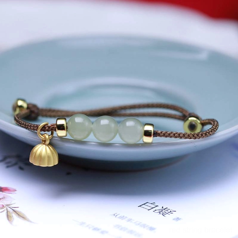 Multicolor woven jade bracelet with lotus seed pod pendant on decorative ceramic backdrop