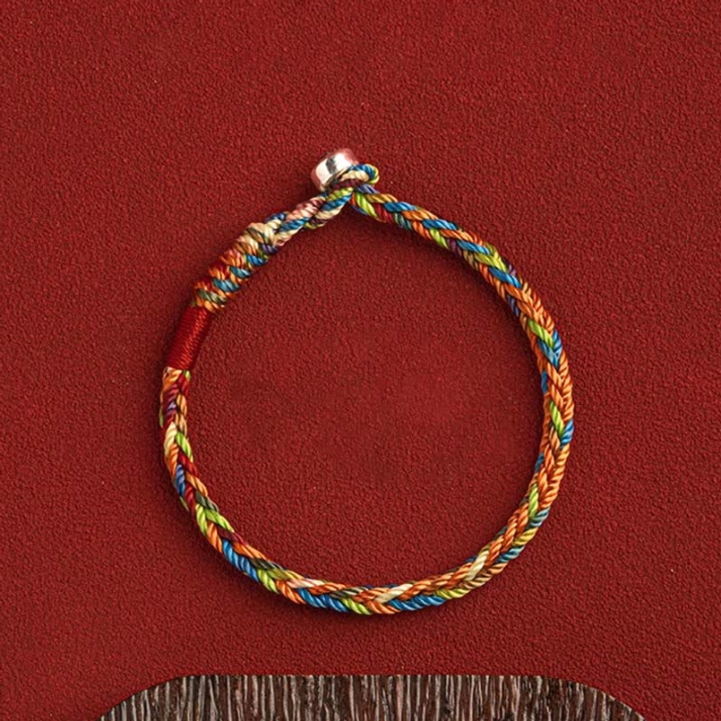 Multicolor woven bracelet with silver clasp and red thread accent on wooden craft display