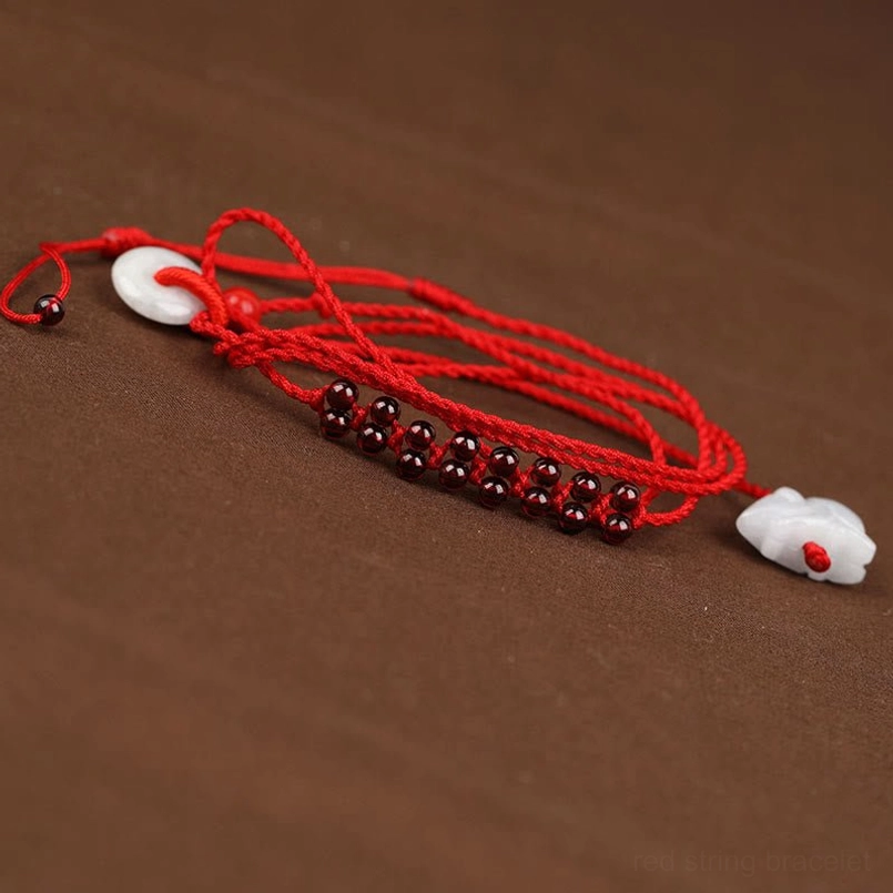 Two Chinese zodiac red string belly chains with garnet beads and jade pendants on dark background