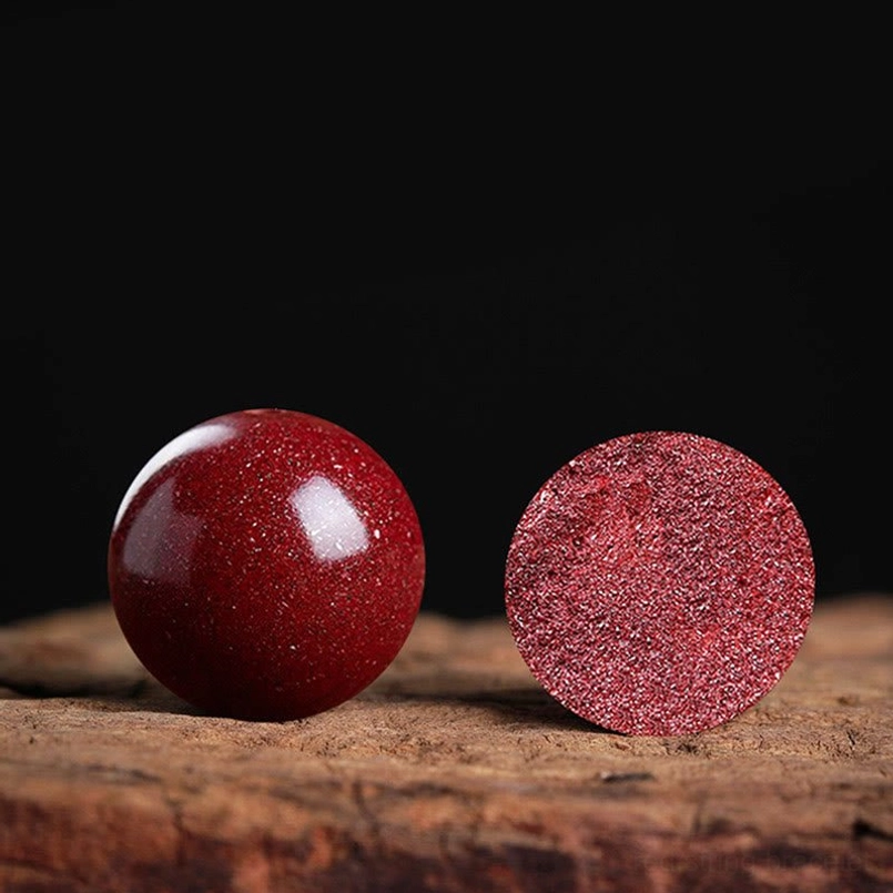 Glossy natural cinnabar bead on wooden surface showing authentic stone texture