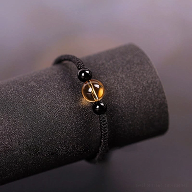 Close up view of black cord bracelet with central citrine flanked by obsidian beads
