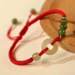 Natural Hetian Jade Peace Buckle Red String Bracelet Close Up On Wooden Coaster